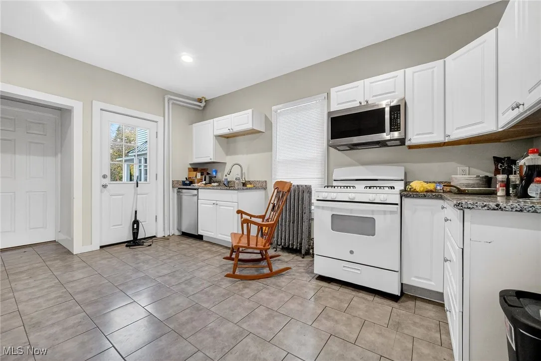 Kitchen featuring white cabinets, dark stone countertops, stainless steel appliances, and light tile patterned floors