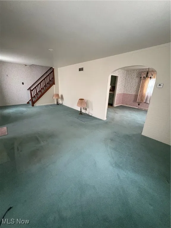 Unfurnished living room with wallpapered walls, arched walkways, carpet flooring, and stairway
