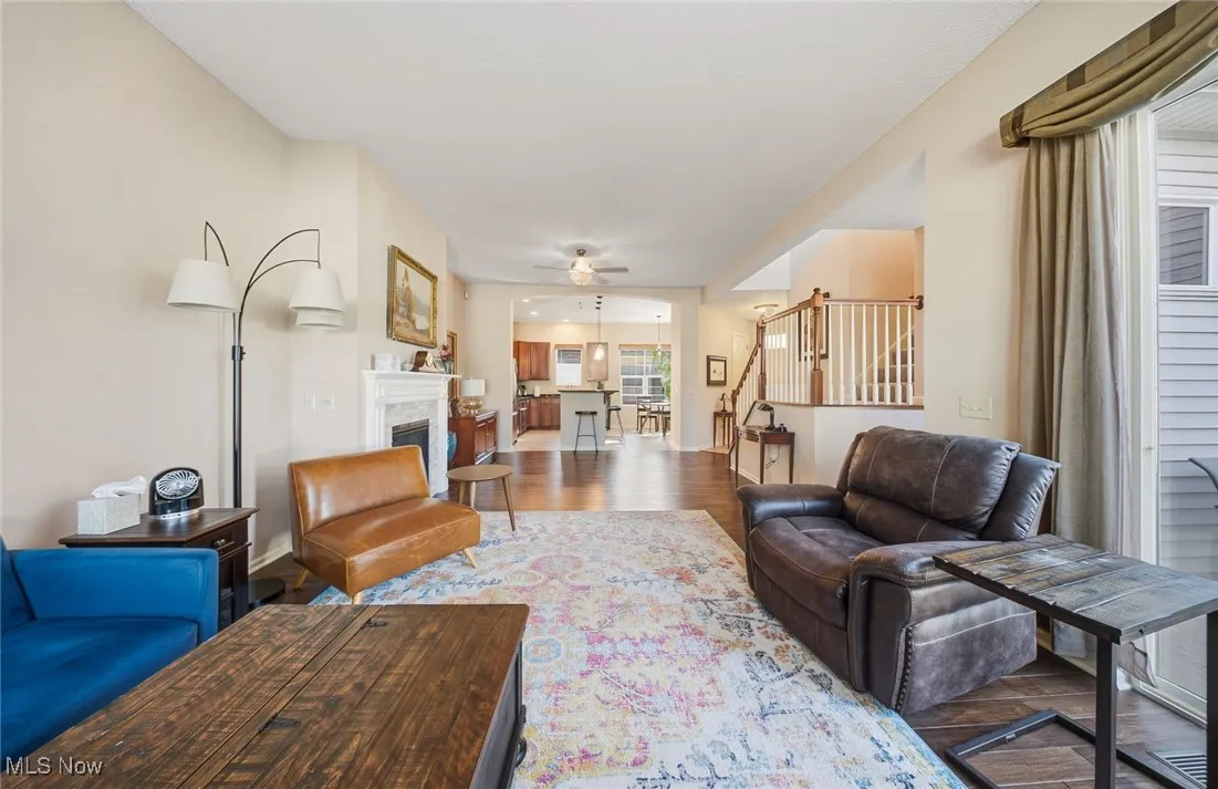 Living area featuring a glass covered fireplace, ceiling fan, wood finished floors, and stairway