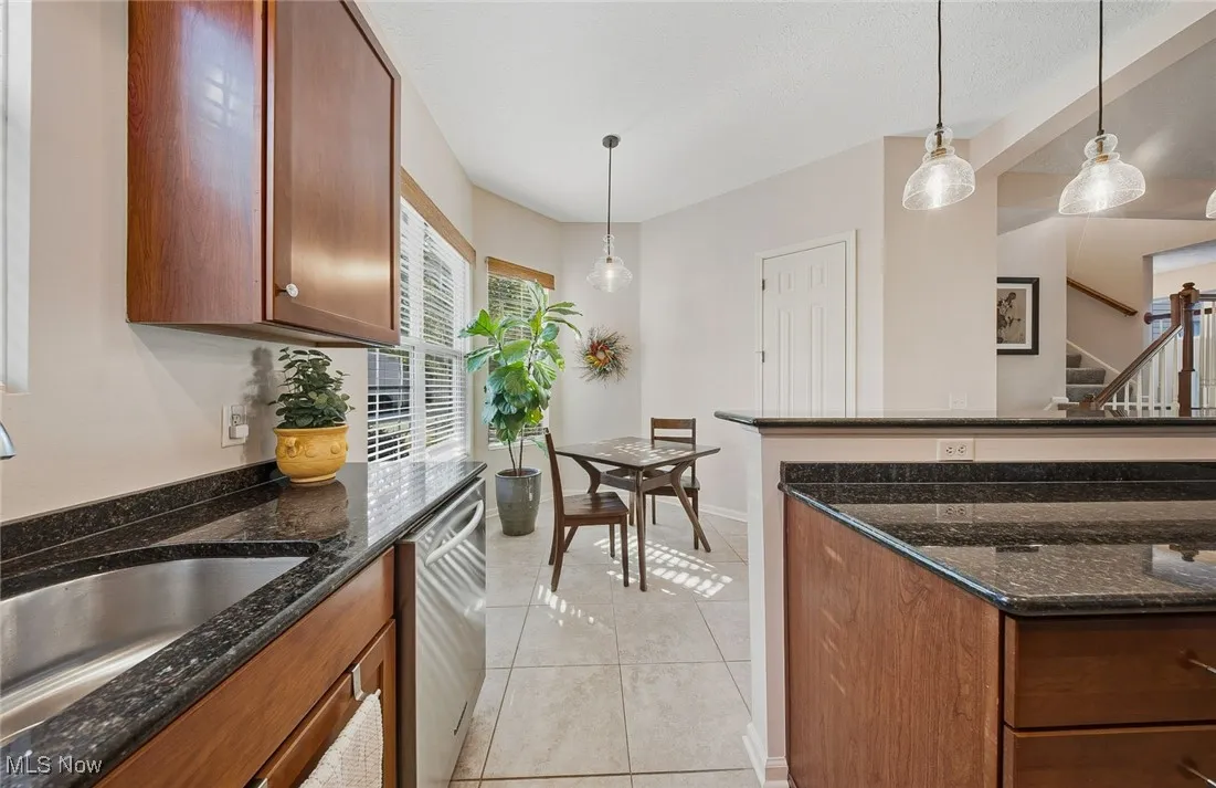 Kitchen with dark stone countertops, pendant lighting, brown cabinets, dishwasher, and light tile patterned flooring