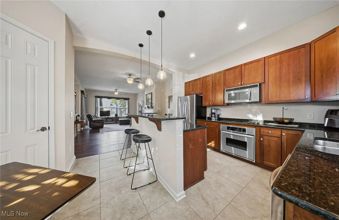 Kitchen with a kitchen breakfast bar, hanging light fixtures, appliances with stainless steel finishes, light tile patterned floors, and a ceiling fan