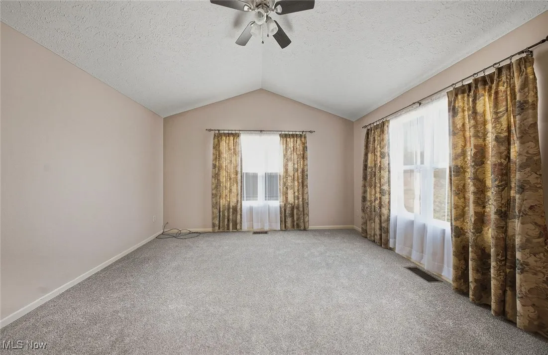 Carpeted spare room with vaulted ceiling, a textured ceiling, and a ceiling fan