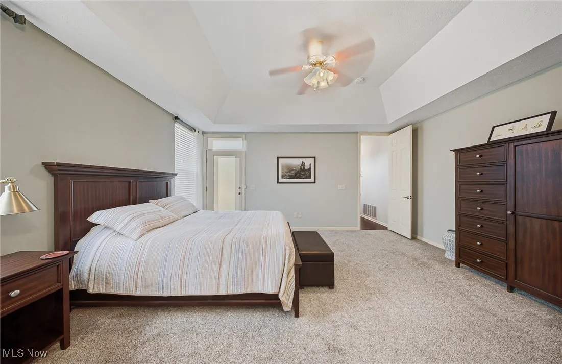 Bedroom featuring light colored carpet, ceiling fan, and a tray ceiling
