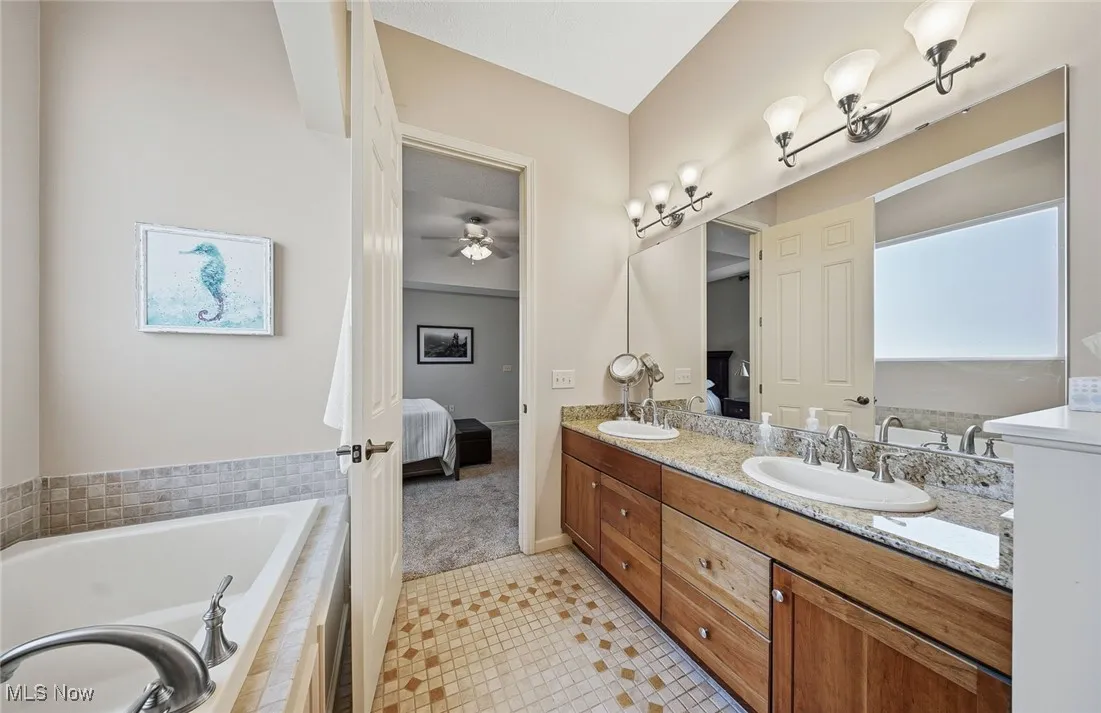 Full bath featuring ensuite bathroom, double vanity, a garden tub, ceiling fan, and light tile patterned floors