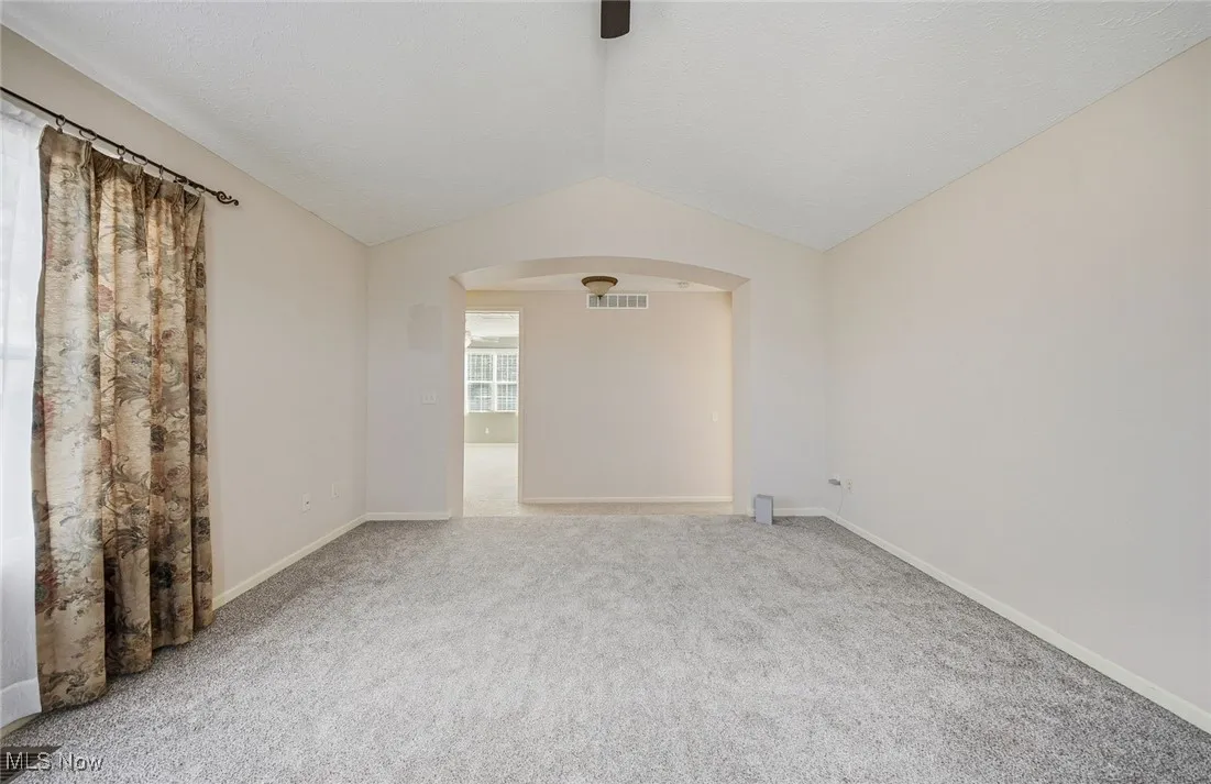 Unfurnished room featuring vaulted ceiling, arched walkways, and light colored carpet