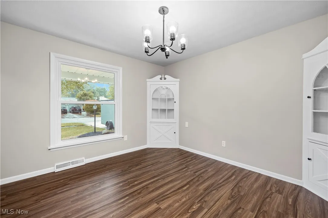 Unfurnished dining area featuring a chandelier and dark wood-style flooring