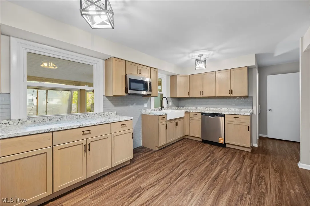 Kitchen featuring light brown cabinets, decorative backsplash, dark wood finished floors, appliances with stainless steel finishes, and light stone counters