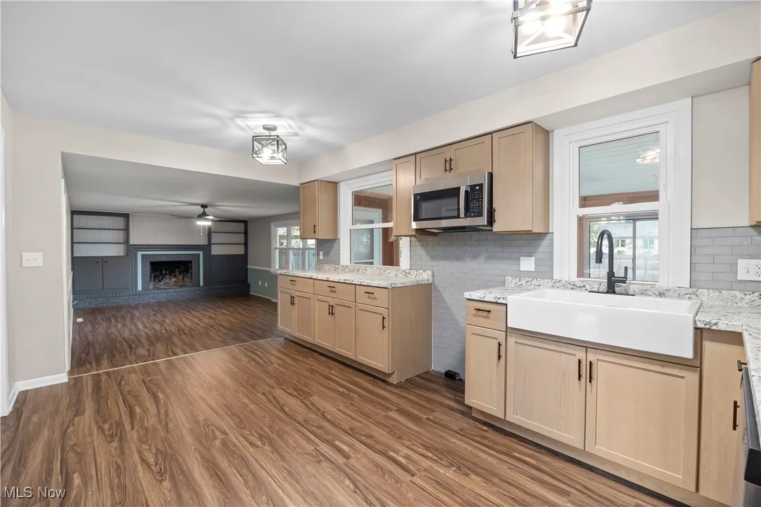 Kitchen featuring a brick fireplace, light brown cabinets, dark wood-type flooring, and decorative backsplash