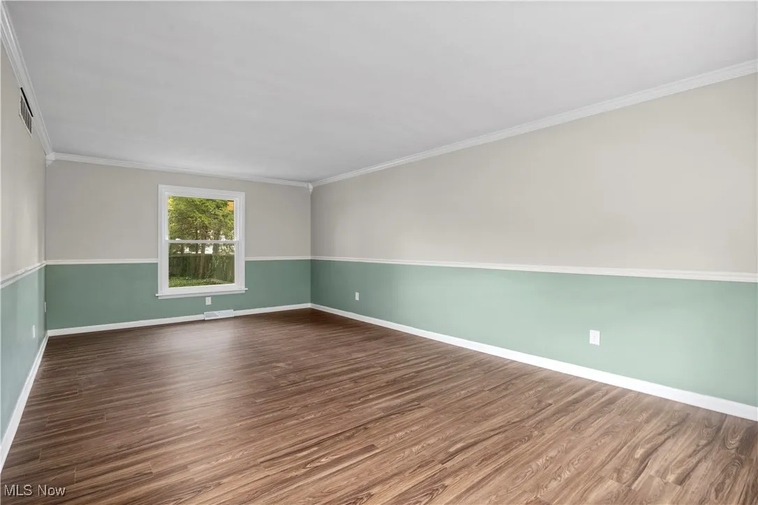 Empty room with dark wood-style flooring and ornamental molding