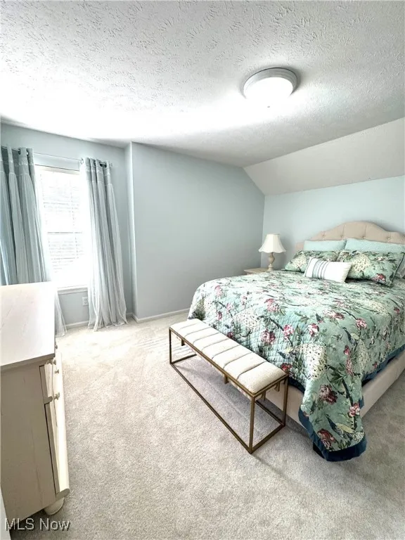 Bedroom with a textured ceiling, carpet floors, and lofted ceiling