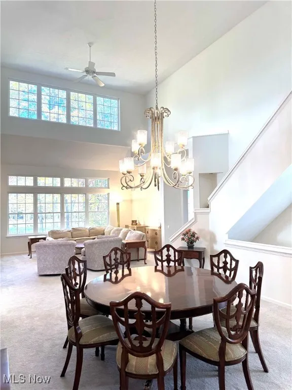 Carpeted dining area with a towering ceiling, a chandelier, and a ceiling fan