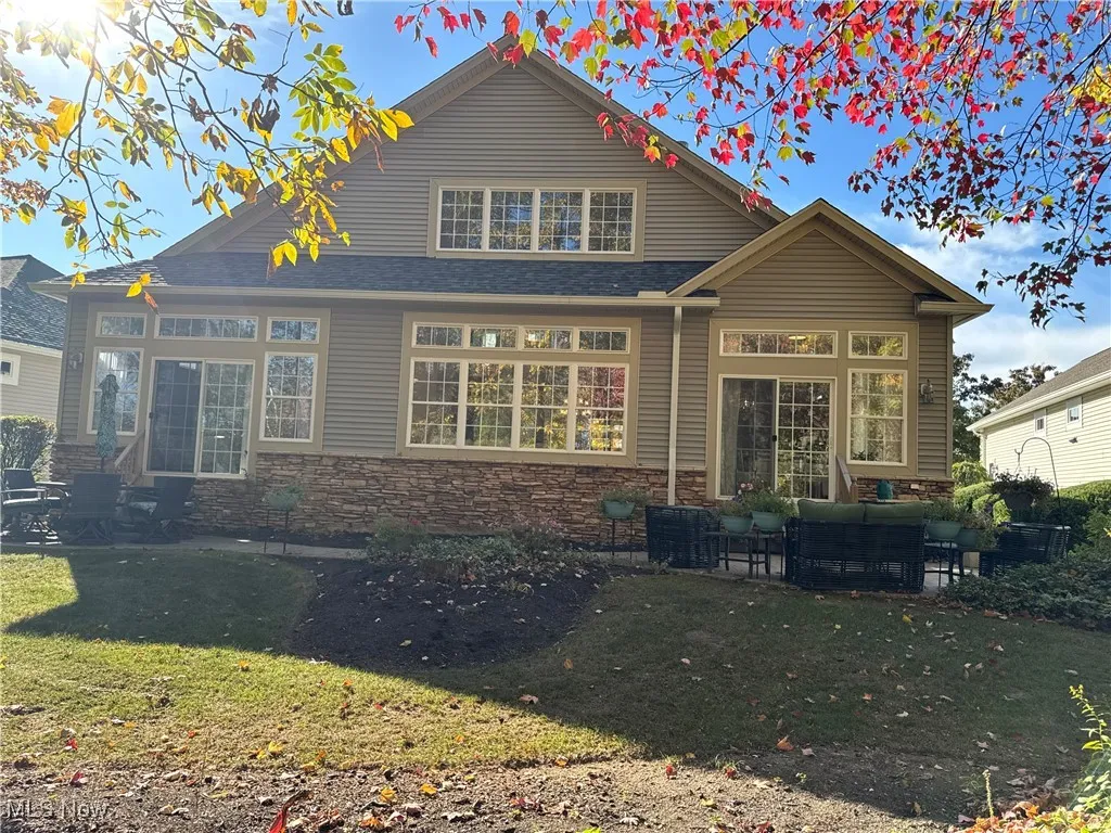 Rear view of property featuring stone siding, a patio, a lawn, and outdoor lounge area
