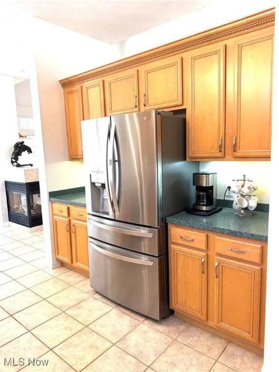 Kitchen featuring dark countertops, stainless steel refrigerator with ice dispenser, light tile patterned flooring, and brown cabinetry