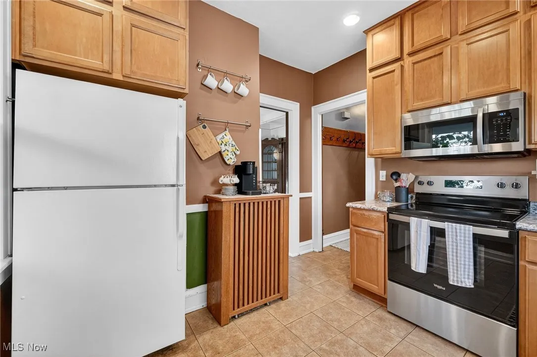 Kitchen featuring stainless steel appliances, light tile patterned floors, and light stone counters
