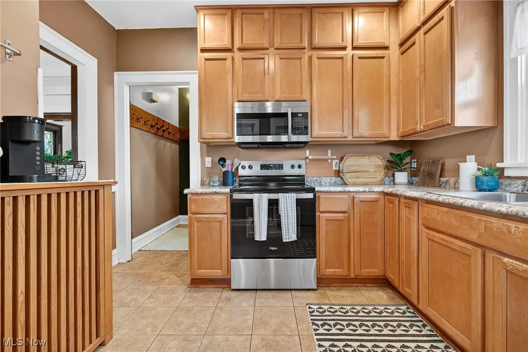 Kitchen with stainless steel appliances, light tile patterned floors, and light stone countertops