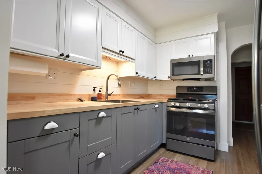 Kitchen with stainless steel appliances, gray cabinets, dark wood-type flooring, wood counters, and white cabinetry
