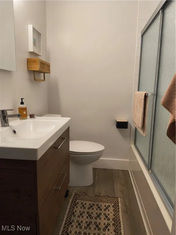 Bathroom with vanity, dark wood-type flooring, and bath / shower combo with glass door