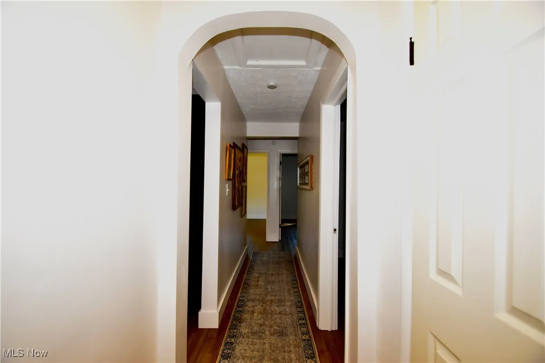 Hall with arched walkways, dark wood-type flooring, and a textured ceiling
