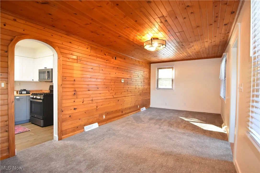 Empty room featuring arched walkways, light carpet, wooden walls, wood ceiling, and ornamental molding