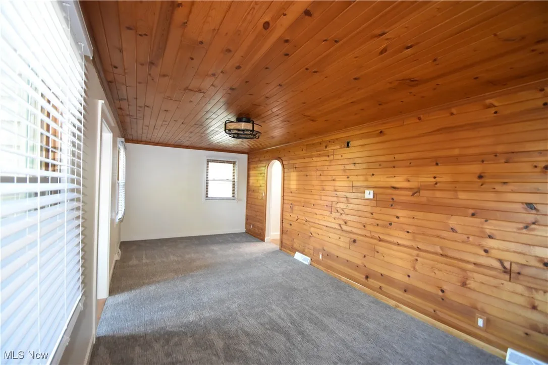 Unfurnished room featuring carpet flooring, wooden walls, arched walkways, ornamental molding, and wooden ceiling