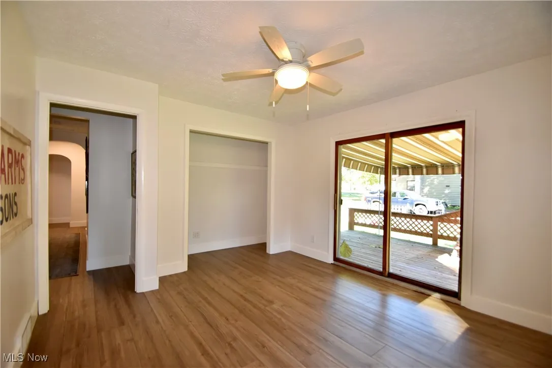 Unfurnished bedroom with access to exterior, wood finished floors, a closet, a ceiling fan, and arched walkways