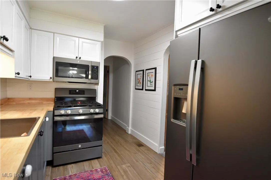 Kitchen with appliances with stainless steel finishes, white cabinetry, wooden counters, arched walkways, and light wood-type flooring