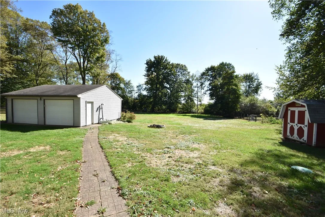 View of green lawn with a storage unit, a detached garage, and view of wooded area