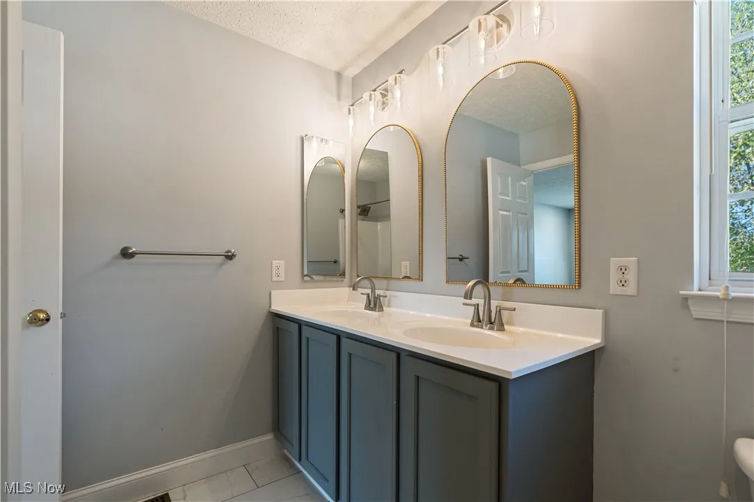Bathroom with double vanity, a textured ceiling, and light tile patterned floors