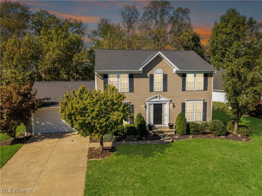 Colonial-style house with a front yard, roof with shingles, driveway, and an attached garage