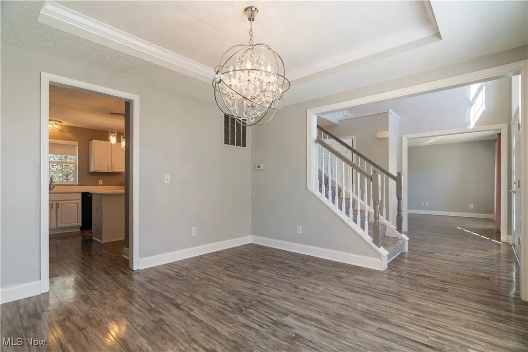 Empty room featuring a tray ceiling, dark wood finished floors, stairway, a chandelier, and a textured ceiling