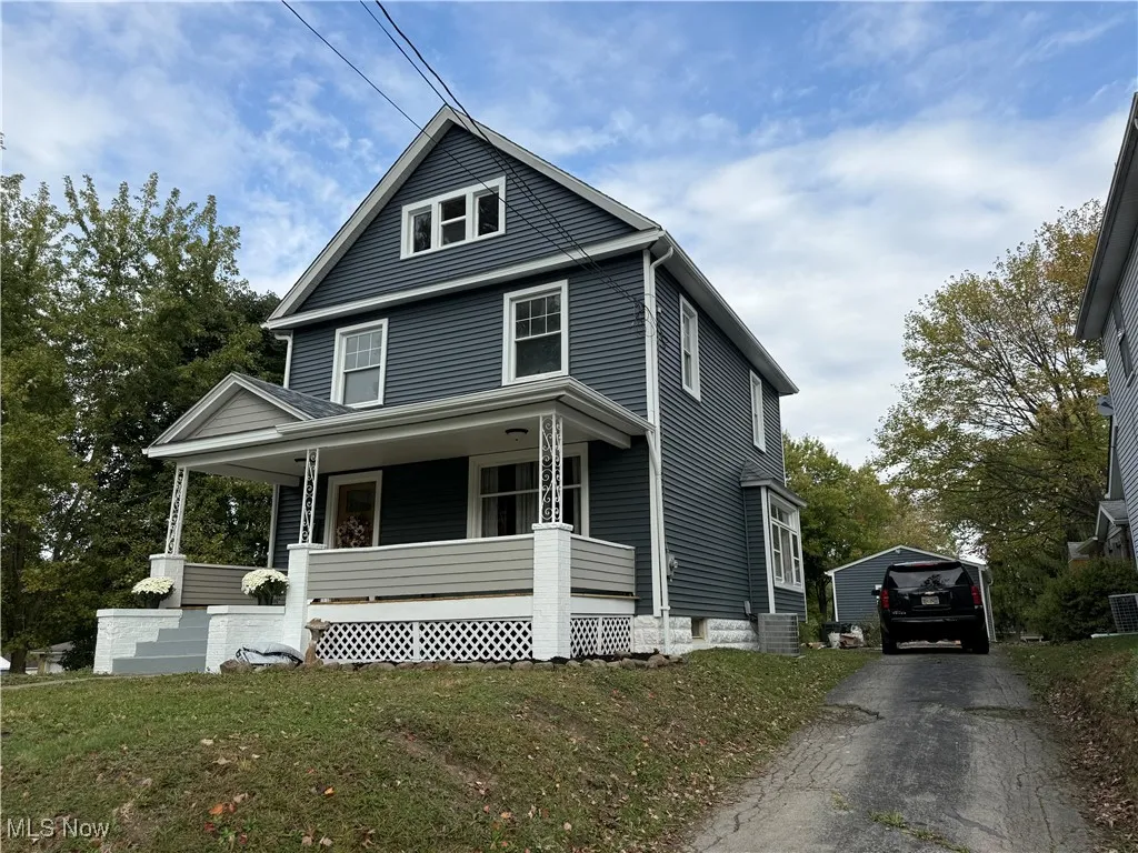 View of front facade with covered porch, a garage, a front lawn, and an outbuilding