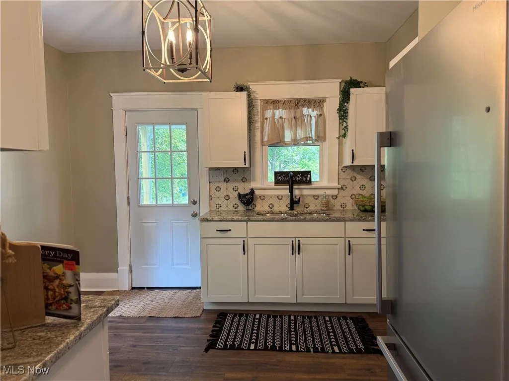 Kitchen with freestanding refrigerator, light stone counters, white cabinets, tasteful backsplash, and dark wood-type flooring