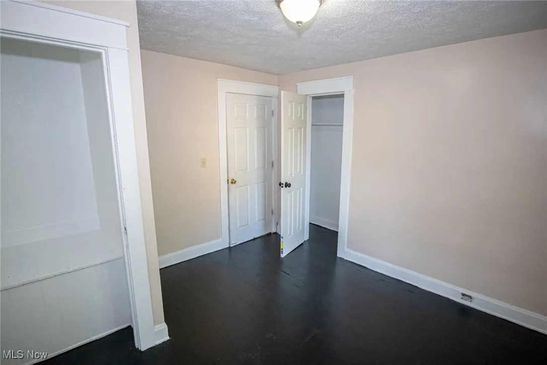 Unfurnished bedroom with a textured ceiling, dark wood-type flooring, and a closet