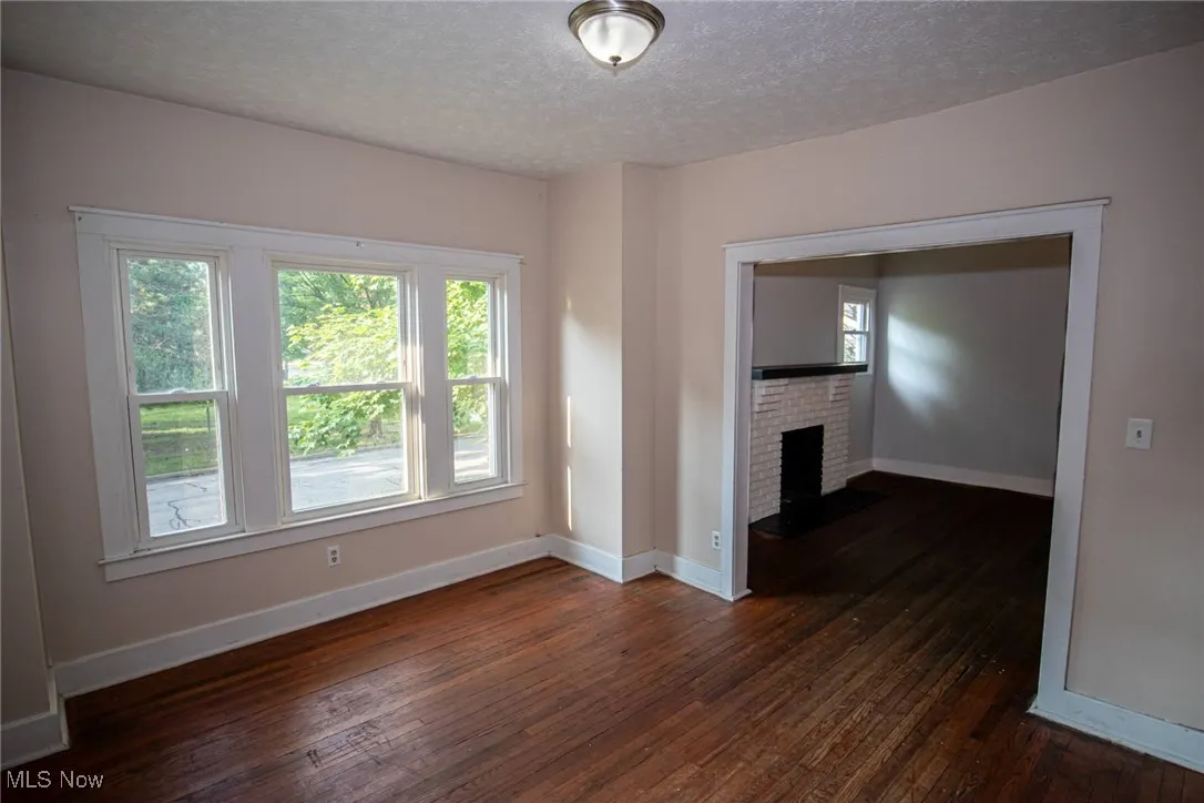 Unfurnished living room with dark wood-style flooring, a textured ceiling, and a brick fireplace