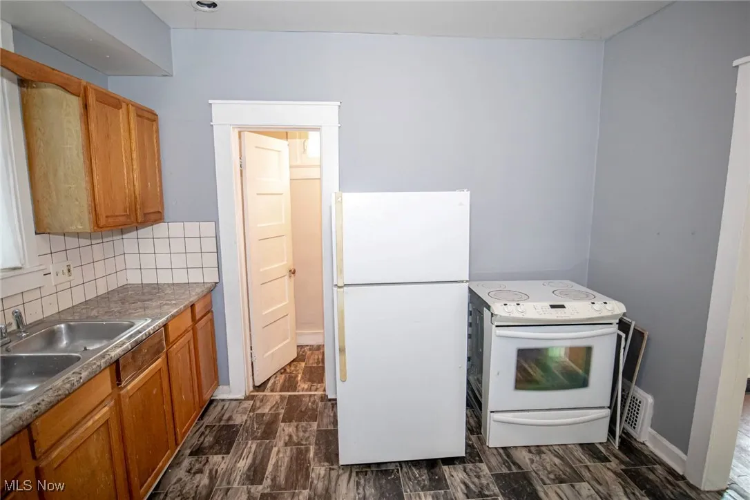 Kitchen featuring white appliances, decorative backsplash, brown cabinets, and wood tiled floors