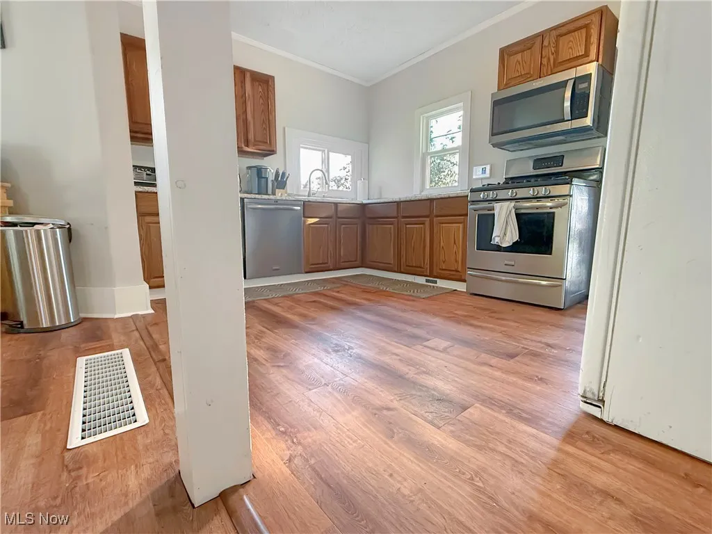 Kitchen with brown cabinets, light countertops, appliances with stainless steel finishes, crown molding, and light wood-type flooring