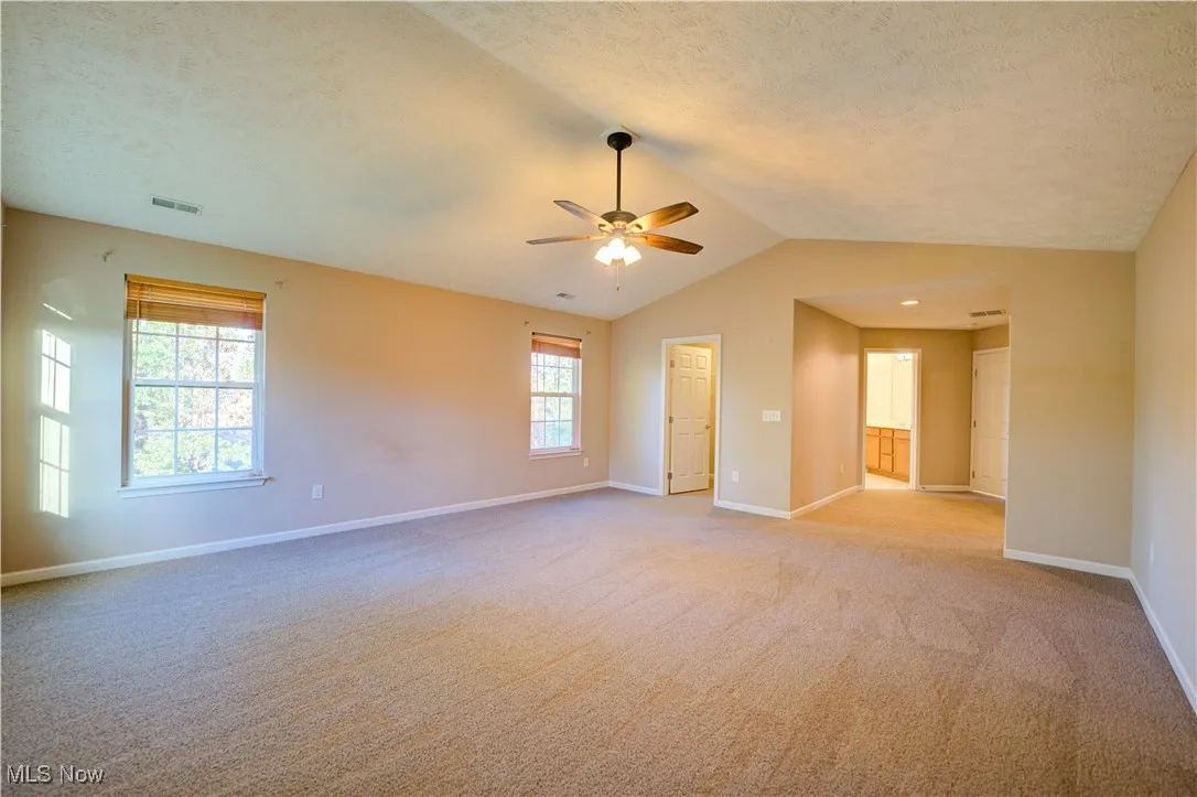 Empty room with light carpet, vaulted ceiling, a textured ceiling, and a ceiling fan