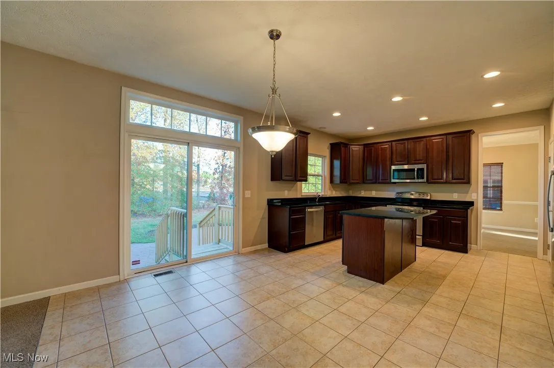 Kitchen featuring dark brown cabinets, stainless steel appliances, hanging light fixtures, light tile patterned floors, and recessed lighting