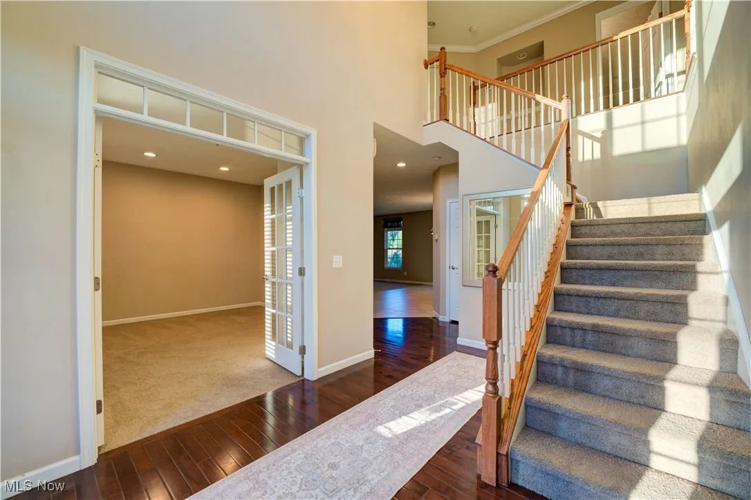 Stairway with hardwood / wood-style floors, a towering ceiling, recessed lighting, ornamental molding, and carpet