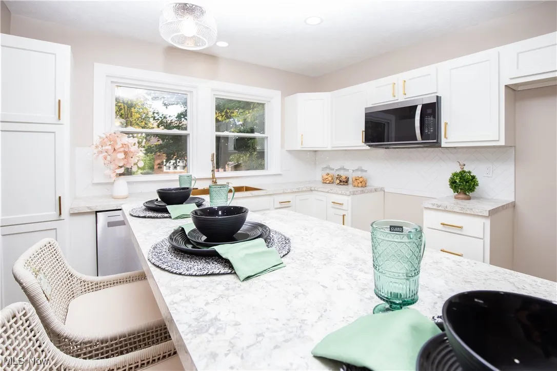 Kitchen featuring backsplash, white cabinetry, stainless steel appliances, recessed lighting, and light stone countertops