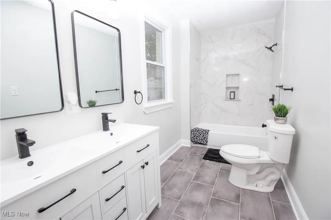 Full bath with double vanity, dark tile patterned flooring, and a combined bath / shower with marble appearance