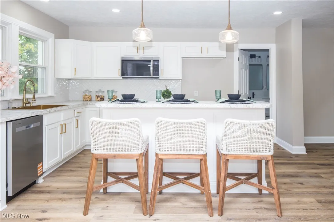 Kitchen featuring a kitchen bar, decorative light fixtures, white cabinetry, appliances with stainless steel finishes, and light wood-style floors