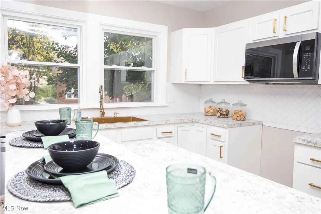 Kitchen featuring decorative backsplash, stainless steel microwave, white cabinetry, and light stone countertops
