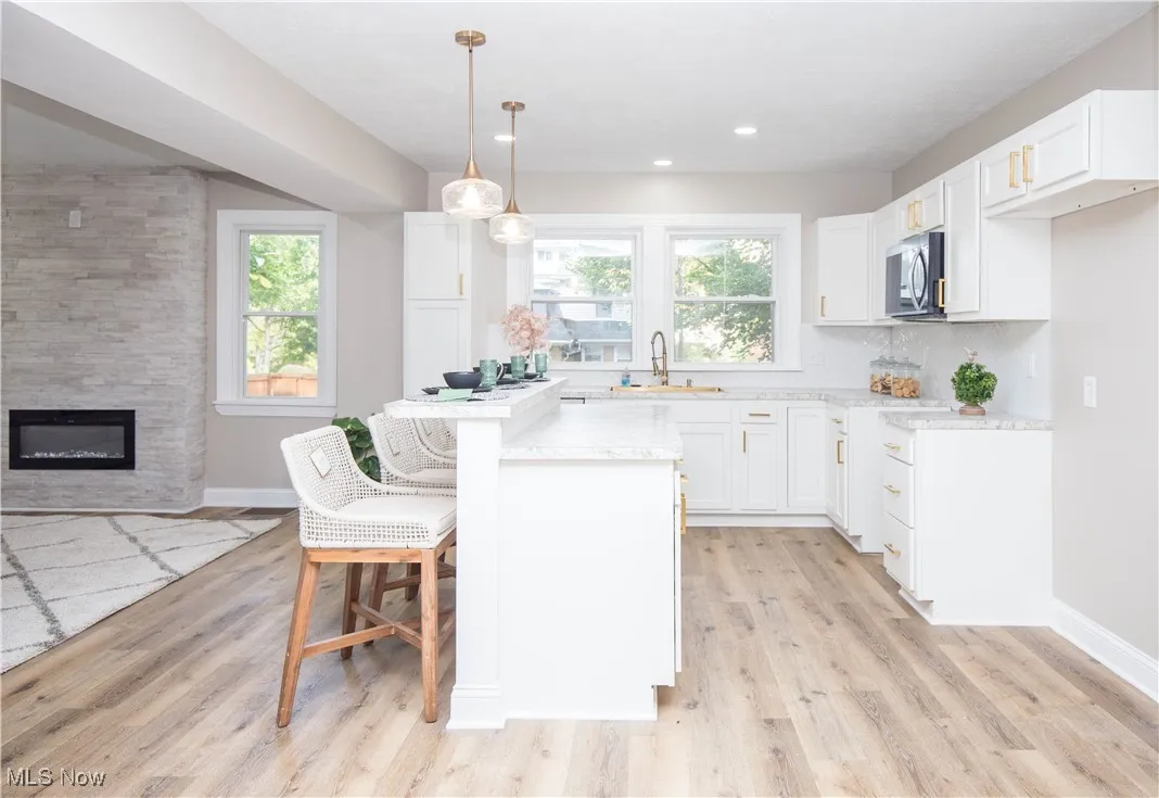 Kitchen featuring a kitchen bar, decorative light fixtures, white cabinetry, stainless steel microwave, and light wood-type flooring