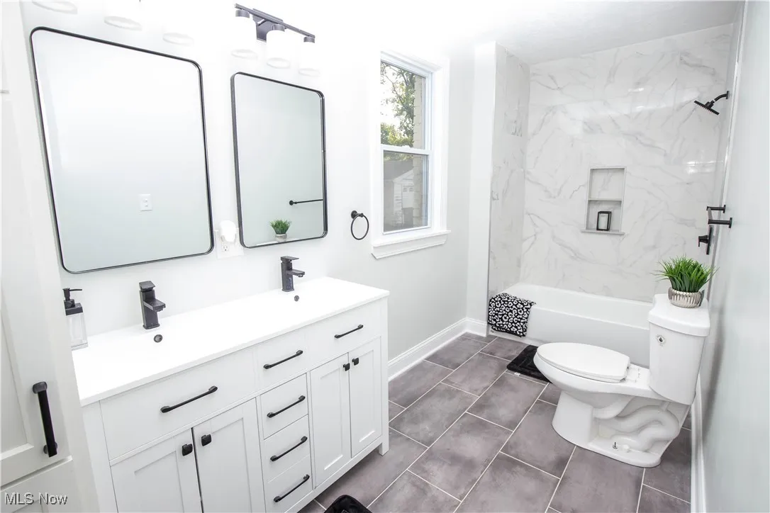 Bathroom featuring double vanity, dark tile patterned floors, and shower / tub combination