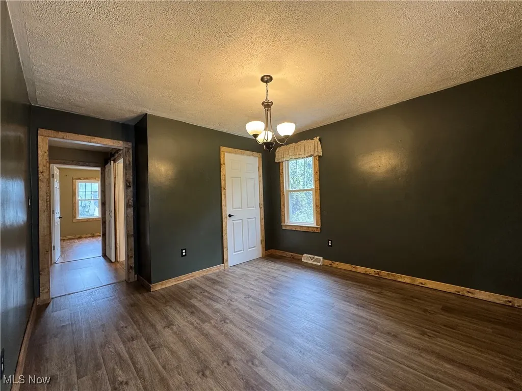 Unfurnished dining area featuring a chandelier, a textured ceiling, and dark wood finished floors