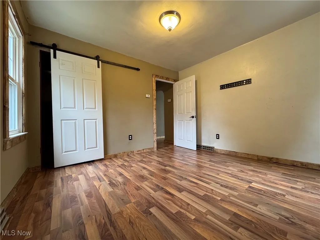 Unfurnished bedroom featuring a barn door and wood finished floors