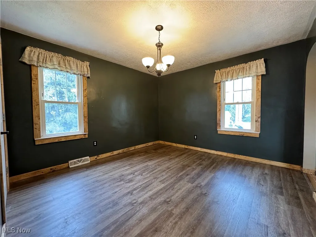 Empty room featuring wood finished floors, a textured ceiling, arched walkways, and a chandelier
