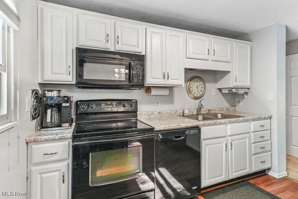 Kitchen featuring black appliances, white cabinetry, wood finished floors, and light stone countertops