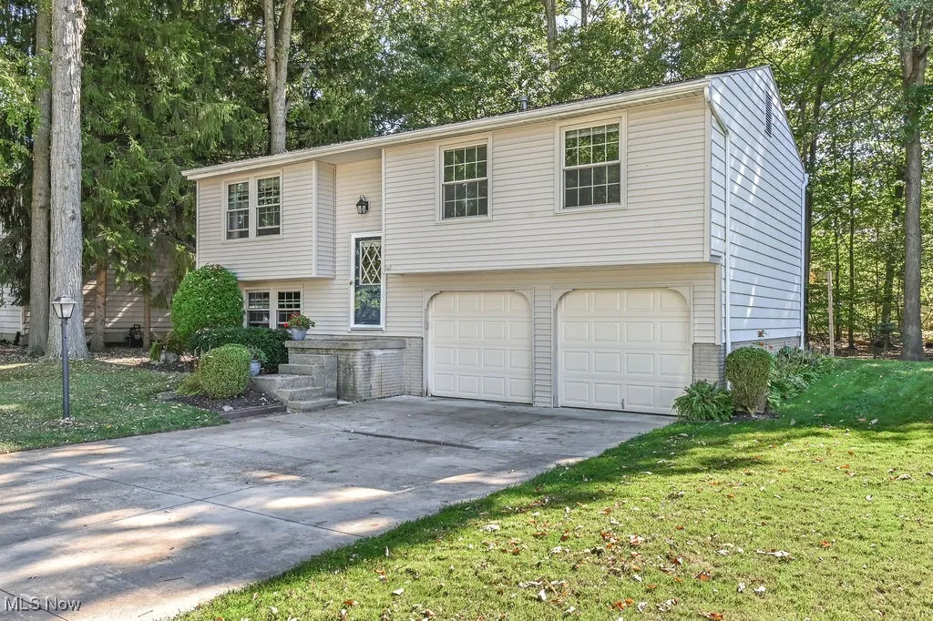 Bilevel with concrete driveway, an attached garage, view of scattered trees, and a front yard